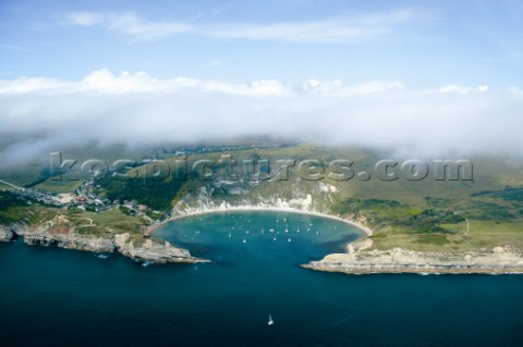 Aerial shot of Lulworth Cove populated by yachts on a sunny cloudy day