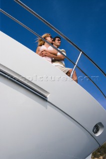 A couple admire the view from the deck of a power boat beneath a clear blue sky