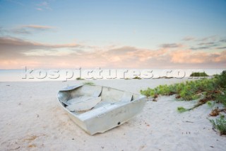 Sunrise over a white sandy beach with foliage and a dinghy