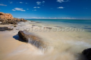 Water breaks on a rock on an unspoilt sandy beach