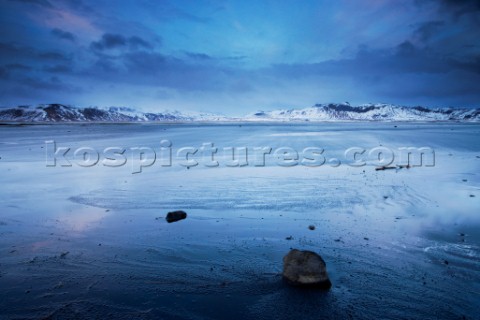 Wind whipping accross the shore on a desolate beach framed by mountains Iceland