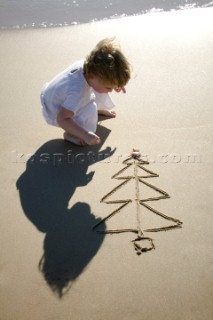 Little girl toddler on a sandy beach adrwing a Christmas Tree Xmas  with shells in Tarifa, Spain, near Gibraltar. (model released)