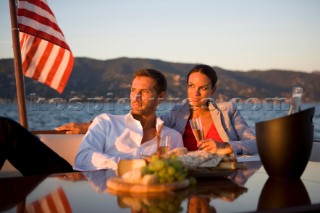 Lifestyle couple having drinks and coctails onboard a Vicem 72 classic motor yacht in the sunset Model Released.