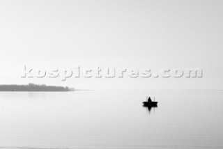 Rowing boat on tranquil lake. Man fishing.
