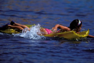 Young girl in a colourful pink bikini paddling on an inflatable  yellow lilo