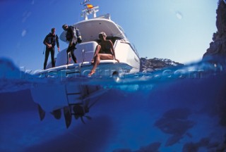 Two scuba divers prepare to enter the water on the back of a power boat