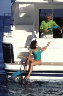 Woman puts on diving fins on the swimming platform of a Fairline Phantom 38 at anchor