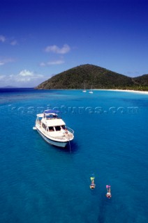Cruising motorboat at anchor in White Bay British Virgin Islands BVI whilst two people snorkel in the blue turquoise water