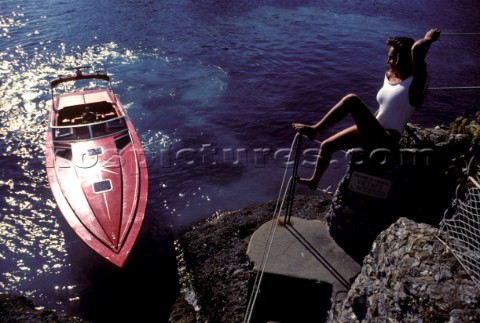 Romantic guy arriving in a fast red powerboat to collect sexy beautiful girl female model in a white