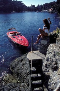Romantic guy arriving in a fast red powerboat to collect sexy beautiful girl female model in a white swimsuit