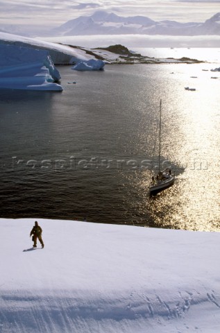 Man standing on icey ridge above anchored yacht 