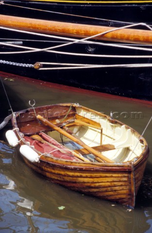 Varnished wooden rowing boat tied alongside yacht 