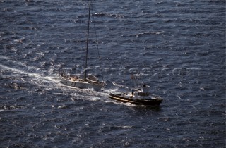 A tug boat tows a stricken sailing yacht into port