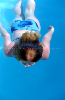 Girl female model swimming underwater with long hair flowing in the turquoise blue water