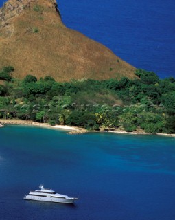 Aerial of superyacht moored in tranquil mooring and bright coloured anchorage with blue water and green trees