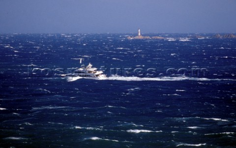 Superyacht My Way passes rocks and a lighthouse in huge rough breaking seas caused by a Mistral wind