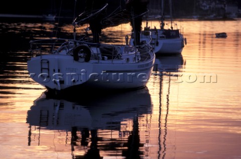 Reflection in calm water of two yachts on the river Hamble at sunrise UK