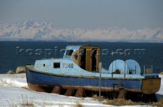 An old wooden fishing boat is laid up on snowy ground
