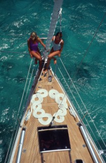 Two women in swimsuits sitting on the bow of a Swan sailboat.