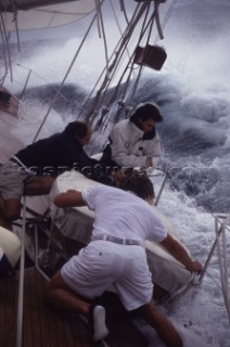 Three crew men working in teamwork secure a dinghy on deck in rough seas and waves