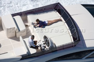 Man driving a powerboat and woman sunbathing.