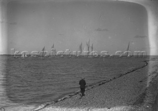 Man walking on the beach during a Big Class regatta off Cowes on the Solent