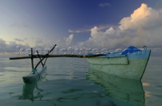 A traditional pacific canoe wonders the waters of Aitutaki Island during sunset, Cook Islands, South Pacific.