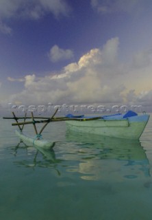 A traditional pacific canoe wonders the waters of Aitutaki Island during sunset, Cook Islands, South Pacific.
