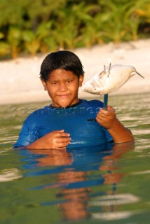A young boy catches fish by spear off Aitutaki Island, Cook Islands, South Pacific.
