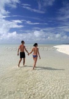 A young couple walk though the clear water of Honeymoon Island, Cook Islands, South Pacific.