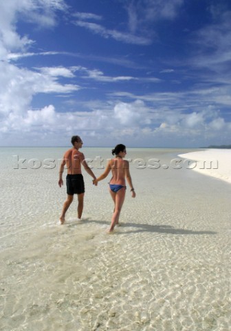 A young couple walk though the clear water of Honeymoon Island Cook Islands South Pacific