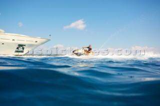 Man jet skiing in the mediterranean sea near a superyacht.