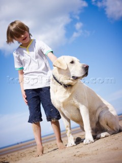 Boy standing on the beach petting a dog
