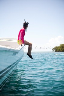 THATCH CAYE, BELIZE. A woman sits on the edge of a boat before snorkeling in the clear waters of the Caribbean.