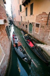 A gondola with tourists sails through a narrow canal in Venice, Italy.