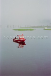 A red lobster boat in the fog at high tide in the Cape Neddick river in York, Maine.