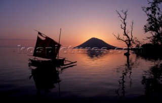 Small fishing sail boat at sunset withManado Tua volcano in backgroundBunaken Island/Indonesia