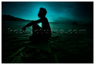 A fisherman sits on the edge of his boat as the sun rises amongst the rock formations that sit in the ocean near the island of Palawan, Southern Philippines.