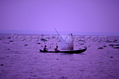 Two men sailing a canoe with a homemade sail at dusk in the Kerala Backwaters India
