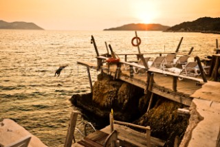 A girl dives off a wooden dock into the Mediterranean Sea at sunset in Kas, Turkey.