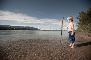 A young boy standing on the shore, looking across the Pend Oreille River, near Sandpoint, Idaho.