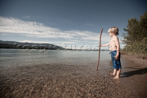A young boy standing on the shore looking across the Pend Oreille River near Sandpoint Idaho