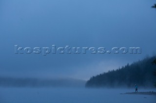 Moody image of a woman walking out on a point in Bowman Lake. Glacier National Park, Montana.