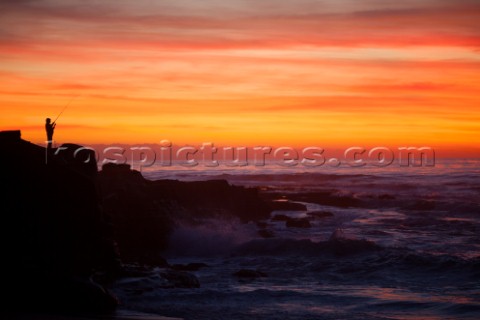 A lone fisherman stands on the rocky shore in La Jolla shore at sunset  San Diego California