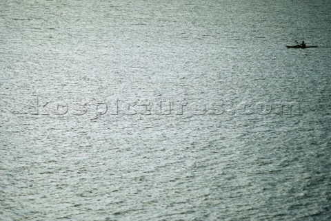 A lone sea kayaker paddles across the shimmering surface of Lake Pend Oreille in Sandpoint Idaho