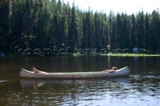 Two teenage boys create the illusion of one long person while lying down in an aluminum canoe in the middle of a small Lake in western Montana. The two boys are cousins and get together at their summer home just outside of Butte