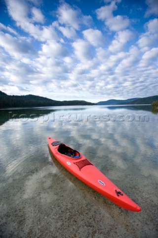 A red sea kayak floats in the shallow reflective waters of Priest Lake in Northern Idaho  The image 