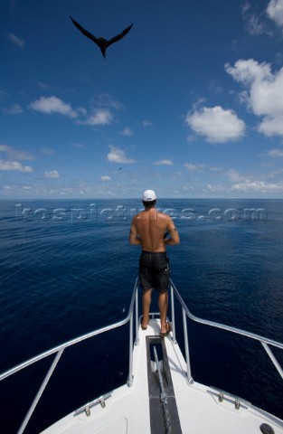 A man fishing off bow of boat as a bird flies through the clouds overhead in the waters off of Costa