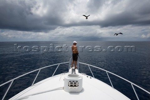 Wide view of a man fishing off the bow of a boat with a bird and dark clouds overhead in Costa Rica