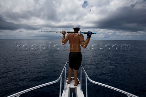 A man with a fishing pole resting on his shoulders looking out at the ocean with dark clouds overhea